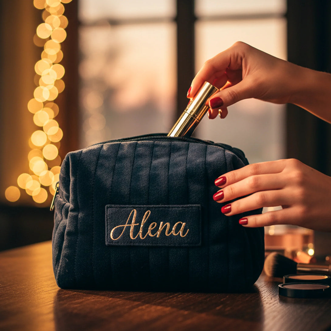 Navy blue personalized makeup bag with name Alena, hand with red nails placing gold lipstick inside